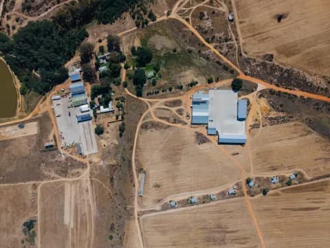 An overhead view of farm buildings, sheds and tracks between planted lands