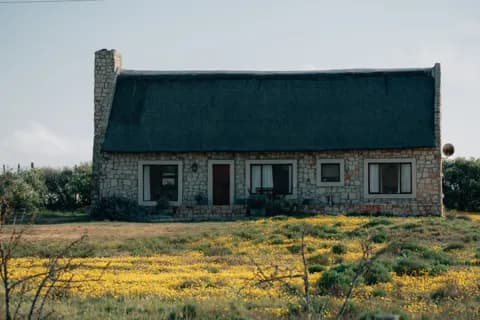 Kliphuis, the Stone Cottage: a thatched stone house with a chimney, in a field of yellow flowers