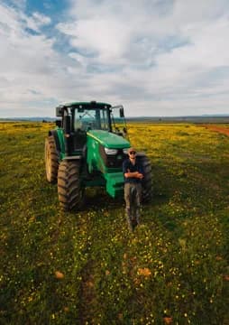 Jan Martin standing in front of a green tractor in a field of yellow flowers