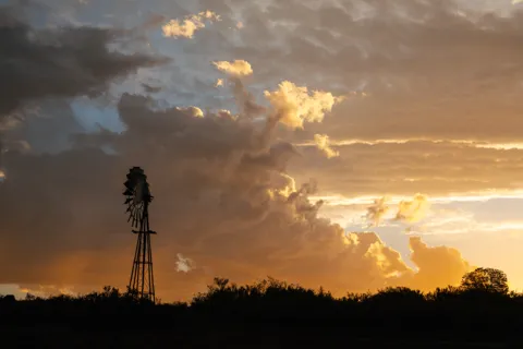 A windmill silhouetted beneath towering evening clouds