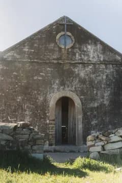 The front of the old stone church: gable, round window and arched door between low stone walls