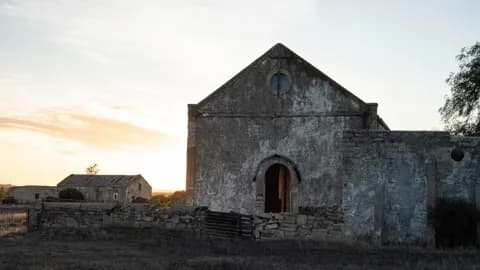 An old stone church with a round window and arched doorway, photographed at dawn