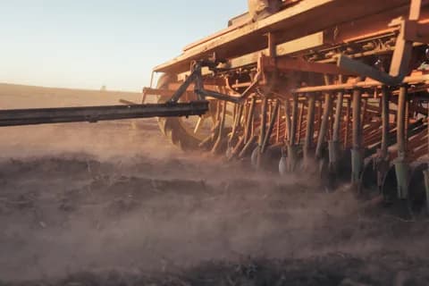 A close view of a planter's tines and discs raising dust in low sun