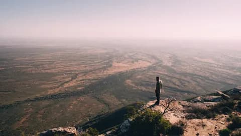 A person standing on the rocky edge of the krans above the vast plain