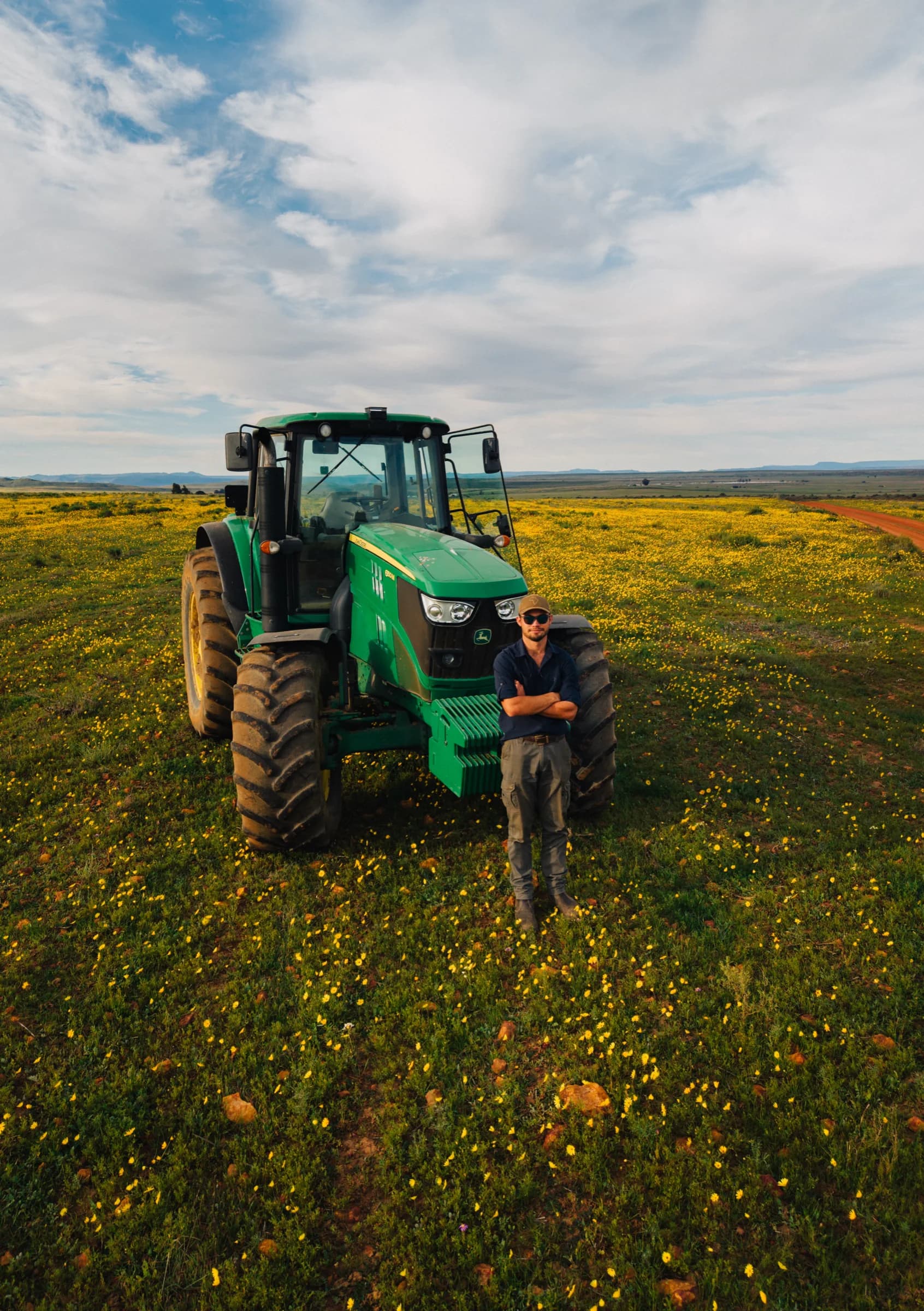 Jan Martin standing in front of a green tractor in a field of yellow flowers