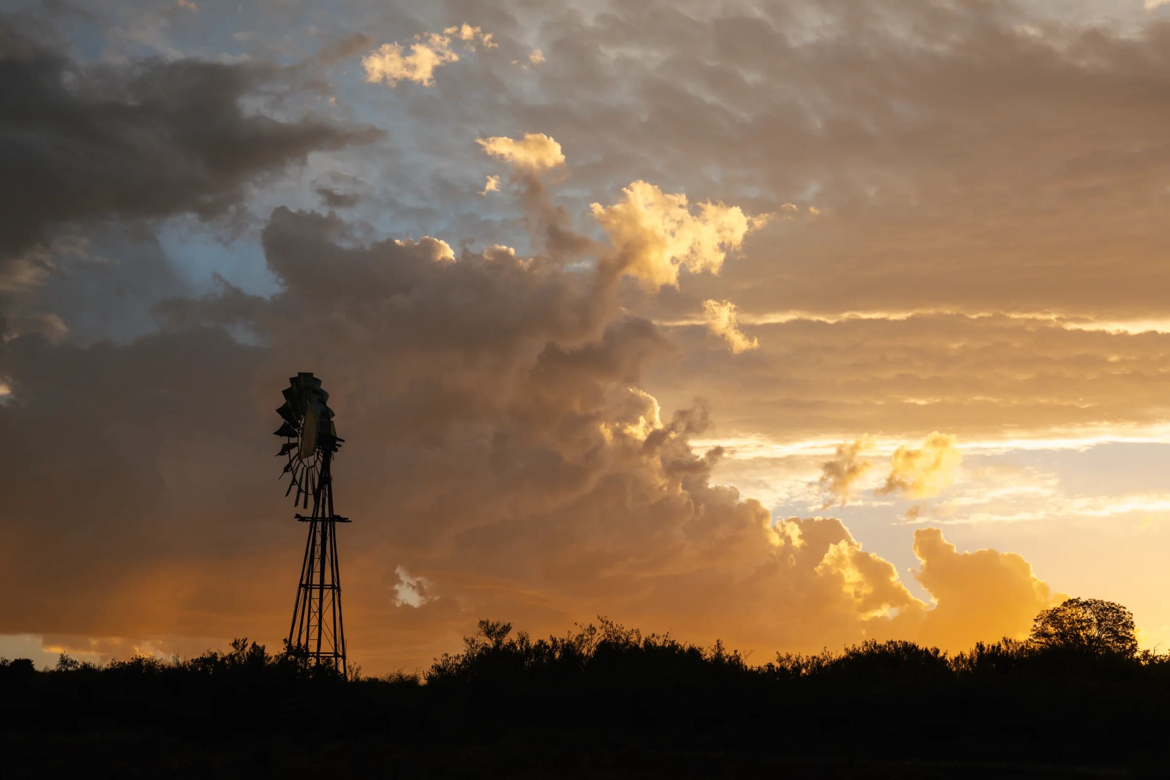 A windmill silhouetted beneath towering evening clouds