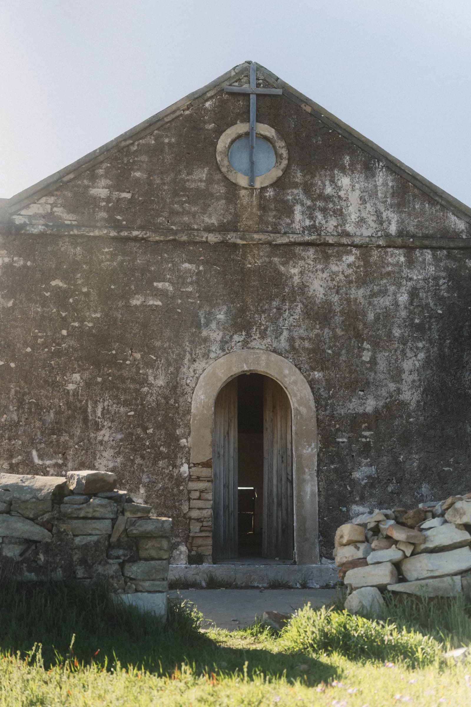 The front of the old stone church: gable, round window and arched door between low stone walls