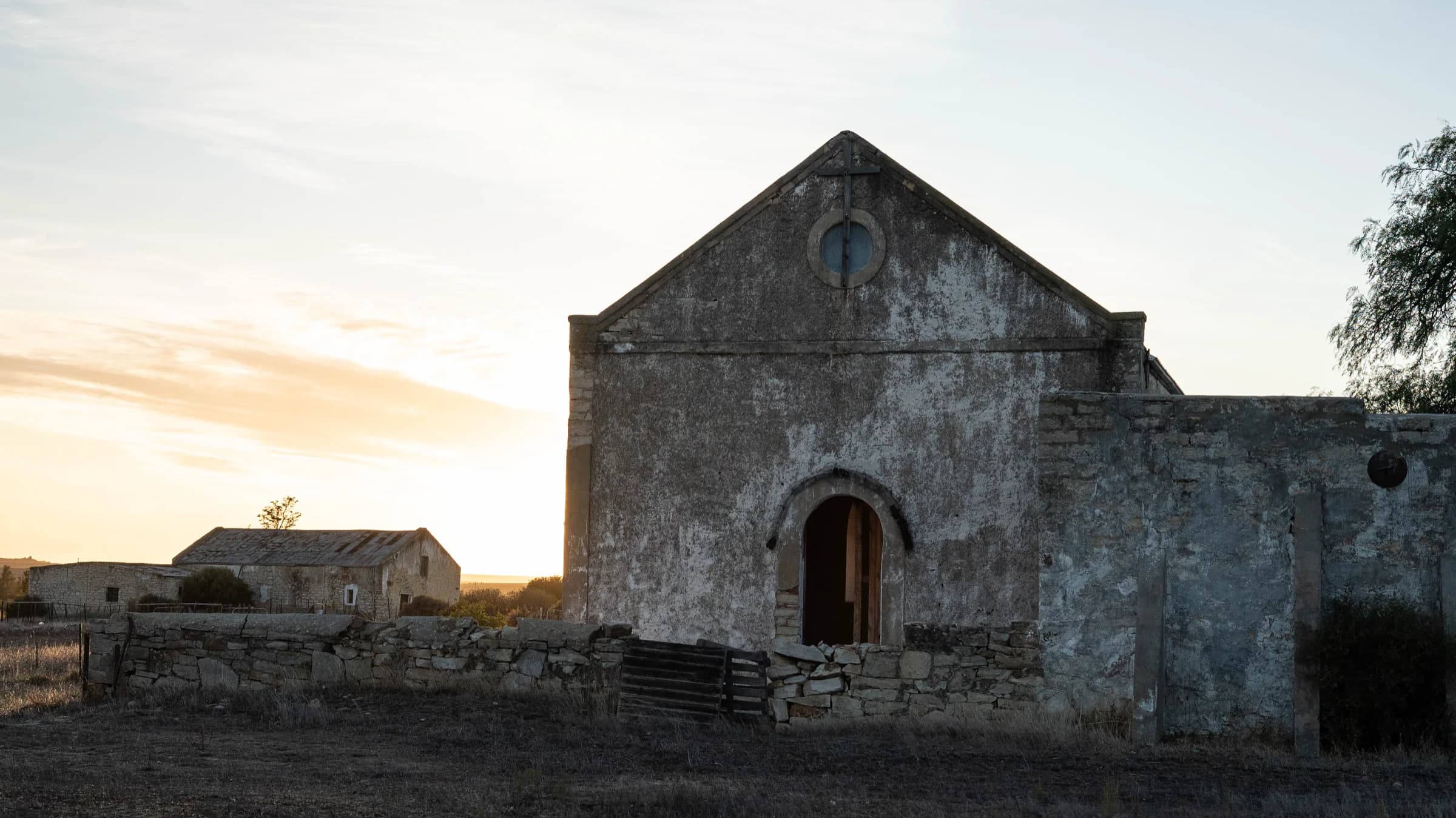 An old stone church with a round window and arched doorway, photographed at dawn