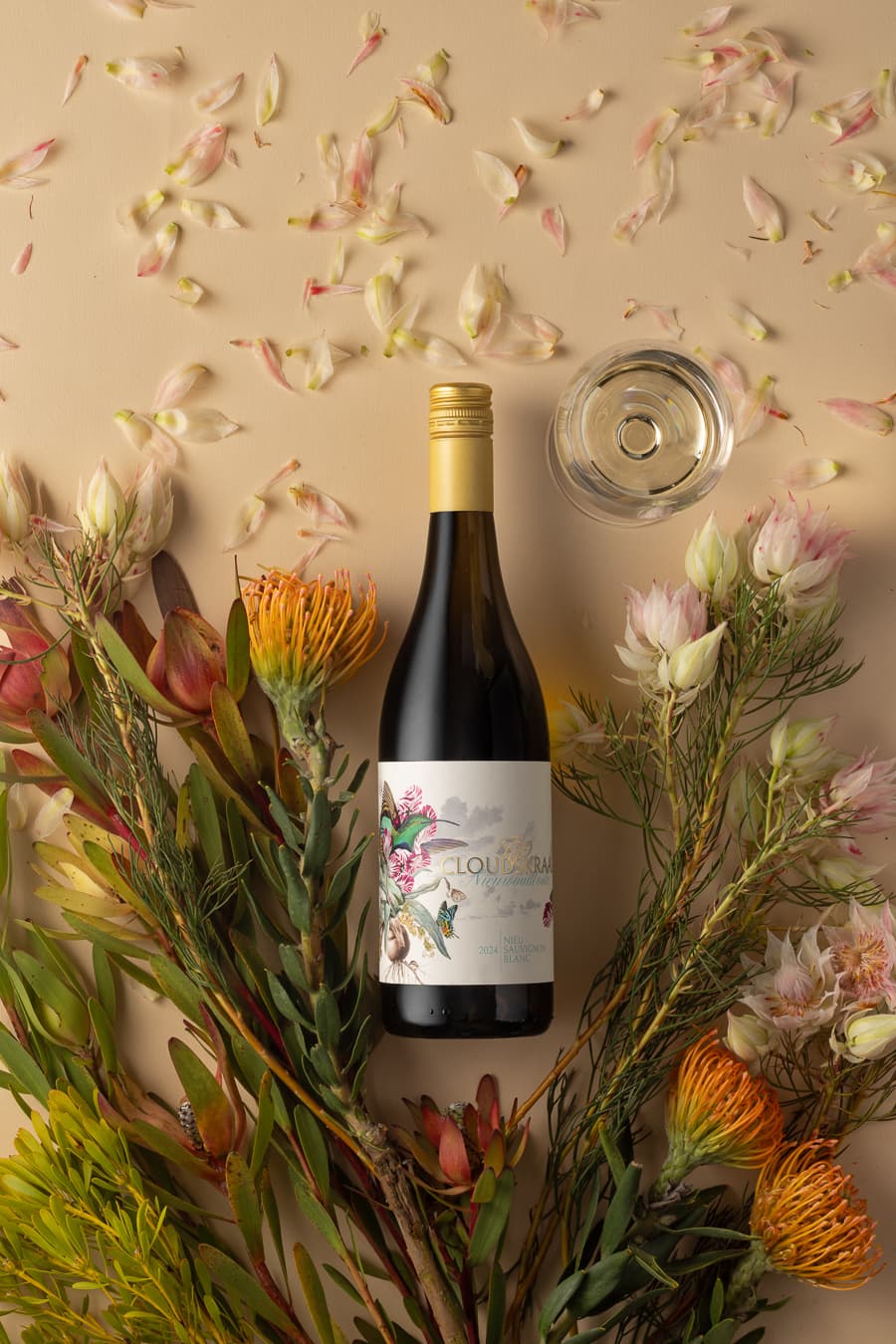 The 2024 bottle and a glass laid among proteas and petals, photographed from above